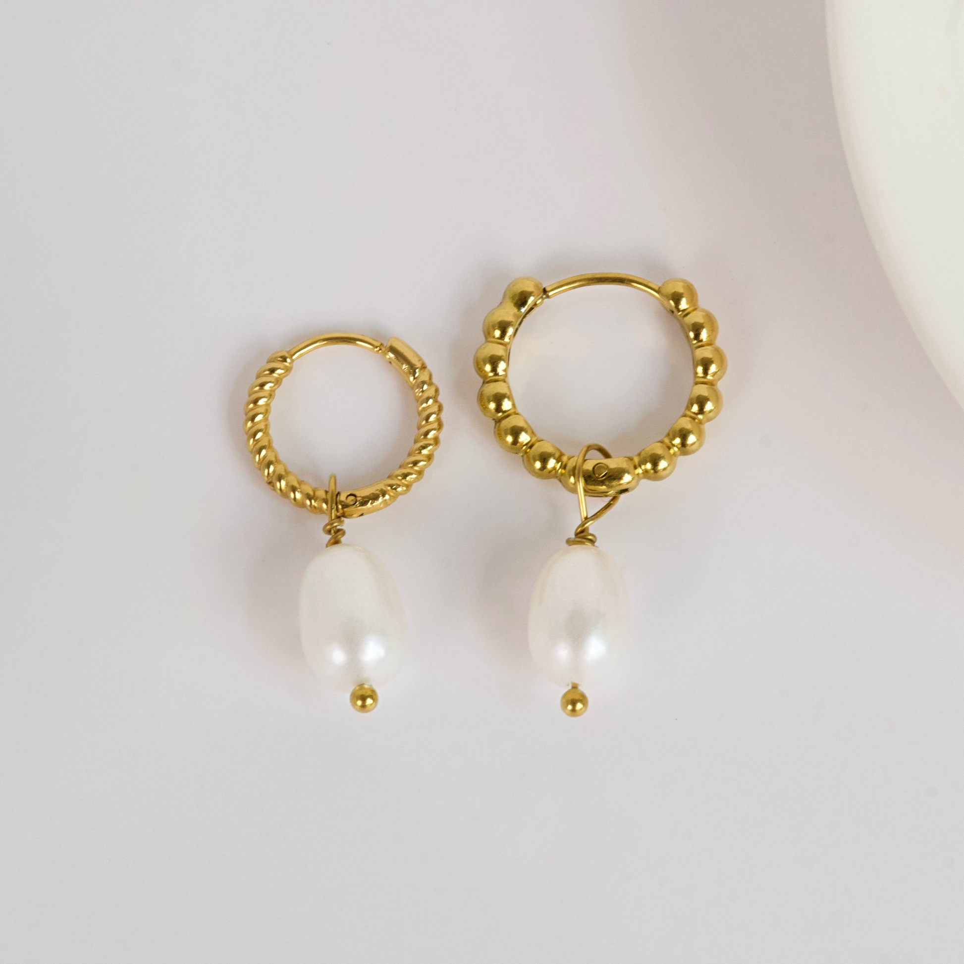 Gold hoop earrings with pearl drops on a light background