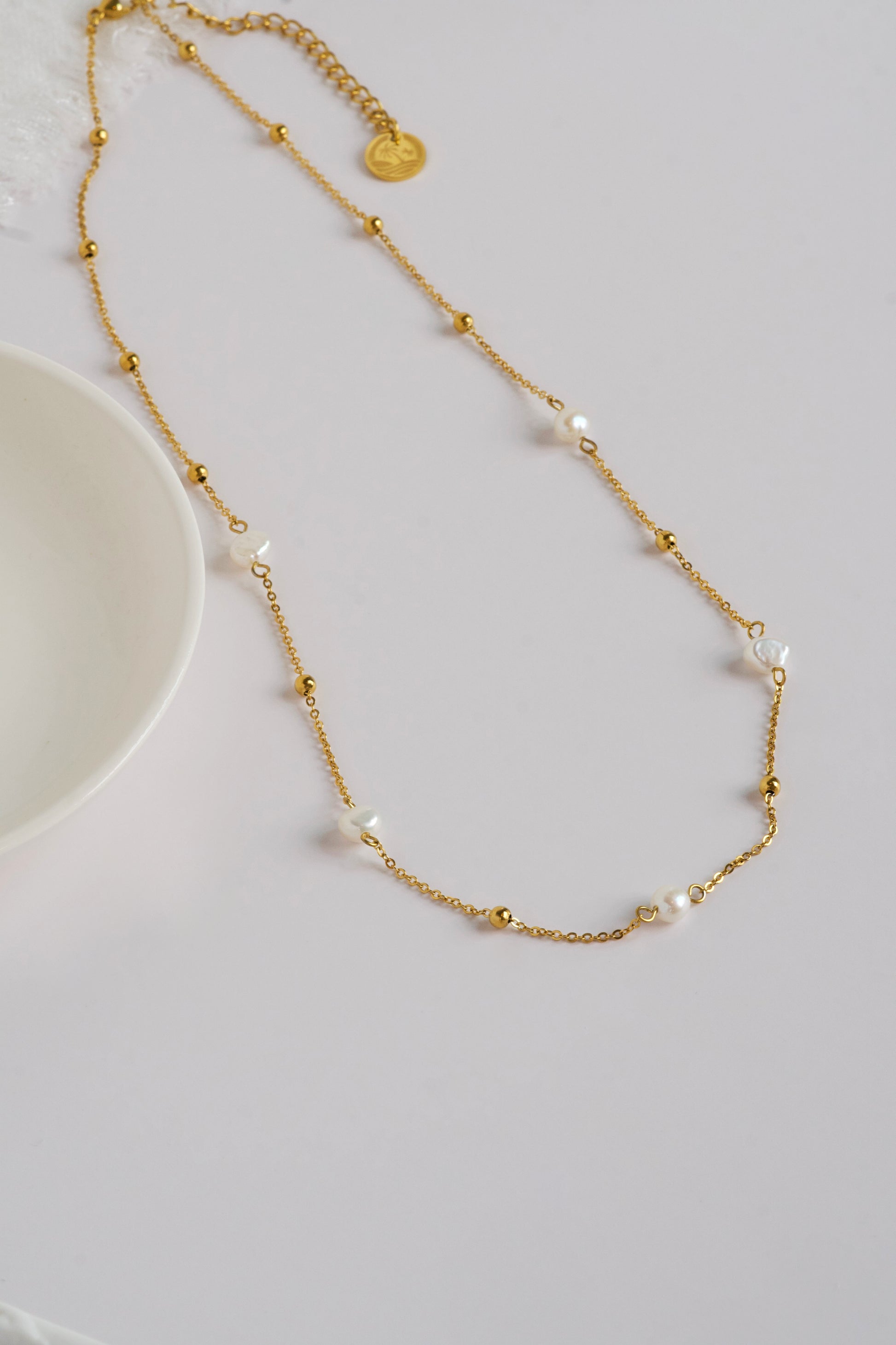 Gold necklace with small beads and pearls on a light gray background